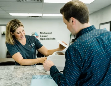 A woman assisting a man that is dropping off a broken printer at Midwest Laser Specialists.